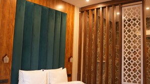 A hotel room with a bed, wooden paneling, a ceiling fan, and a decorative screen. - Hotel Oriva (Aligarh)