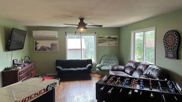 A living room with a foosball table, a television, a couch, and a dartboard.