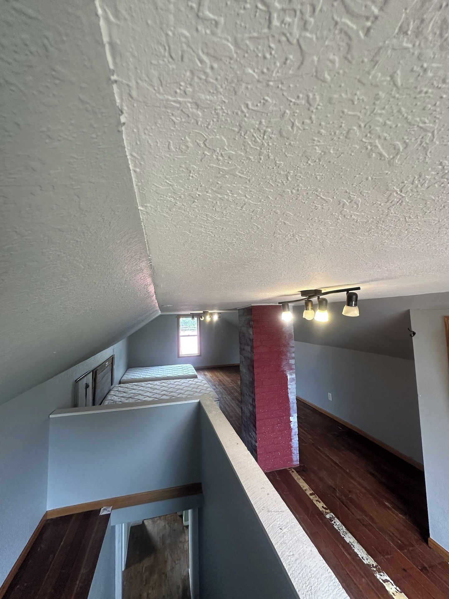 Une pièce avec un plafond en pente, une colonne en briques rouges et un plancher en bois.