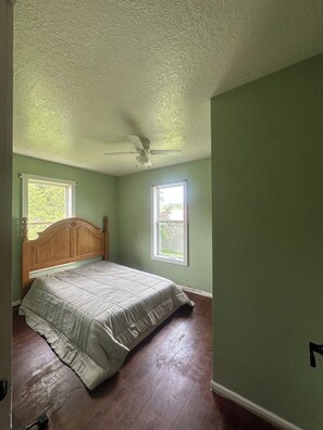A bedroom with a wooden bed, two windows, a ceiling fan, and hardwood flooring. - Rustic Farmhouse on Working WI Wedding Venue (Sparta)