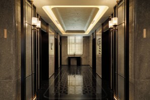 A modern elevator lobby with a reflective floor, a central light fixture, and a glass door with a sign.