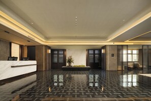 Un moderno vestíbulo de hotel con una recepción, una planta en maceta grande y un área de descanso con dos sillones.
