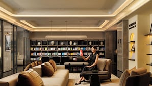 A modern library with leather sofas, a woman reading a book, and bookshelves filled with books and decorative items. - AtourHotelDalianXinghaiSquareRoosevelt (Dalian City)