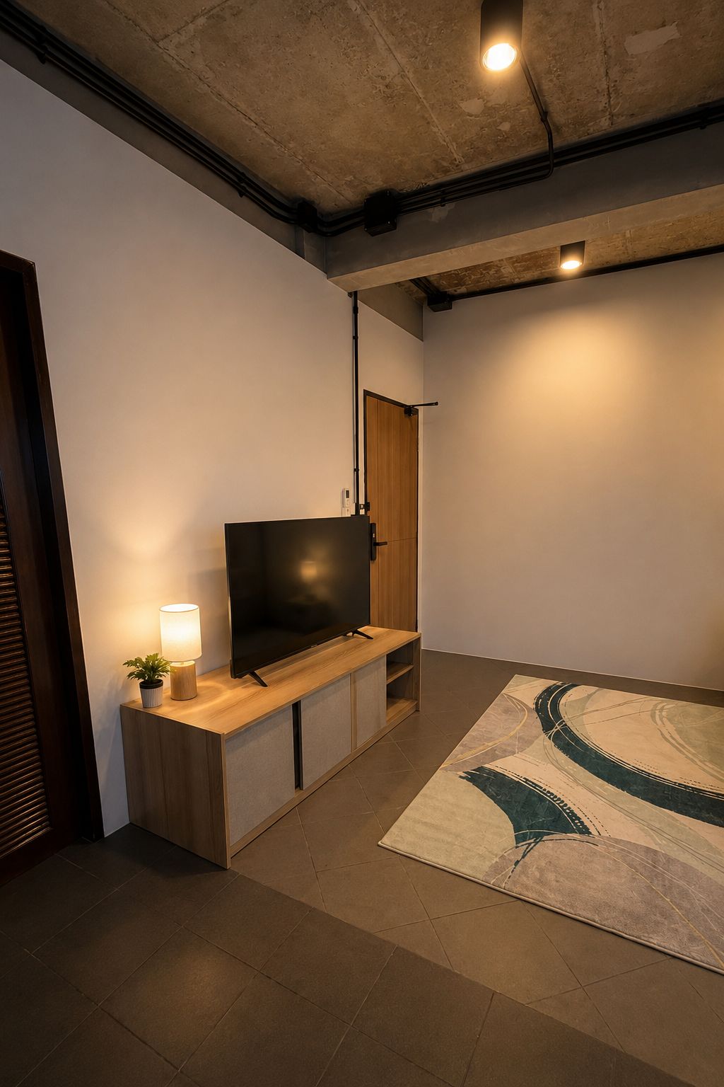 Een moderne woonkamer met een flatscreen televisie, een houten tv-meubel, een lamp en een kamerkleed met een patroon.