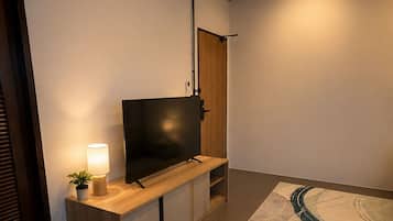 Een moderne woonkamer met een flatscreen televisie, een houten tv-meubel, een lamp en een kamerkleed met een patroon.