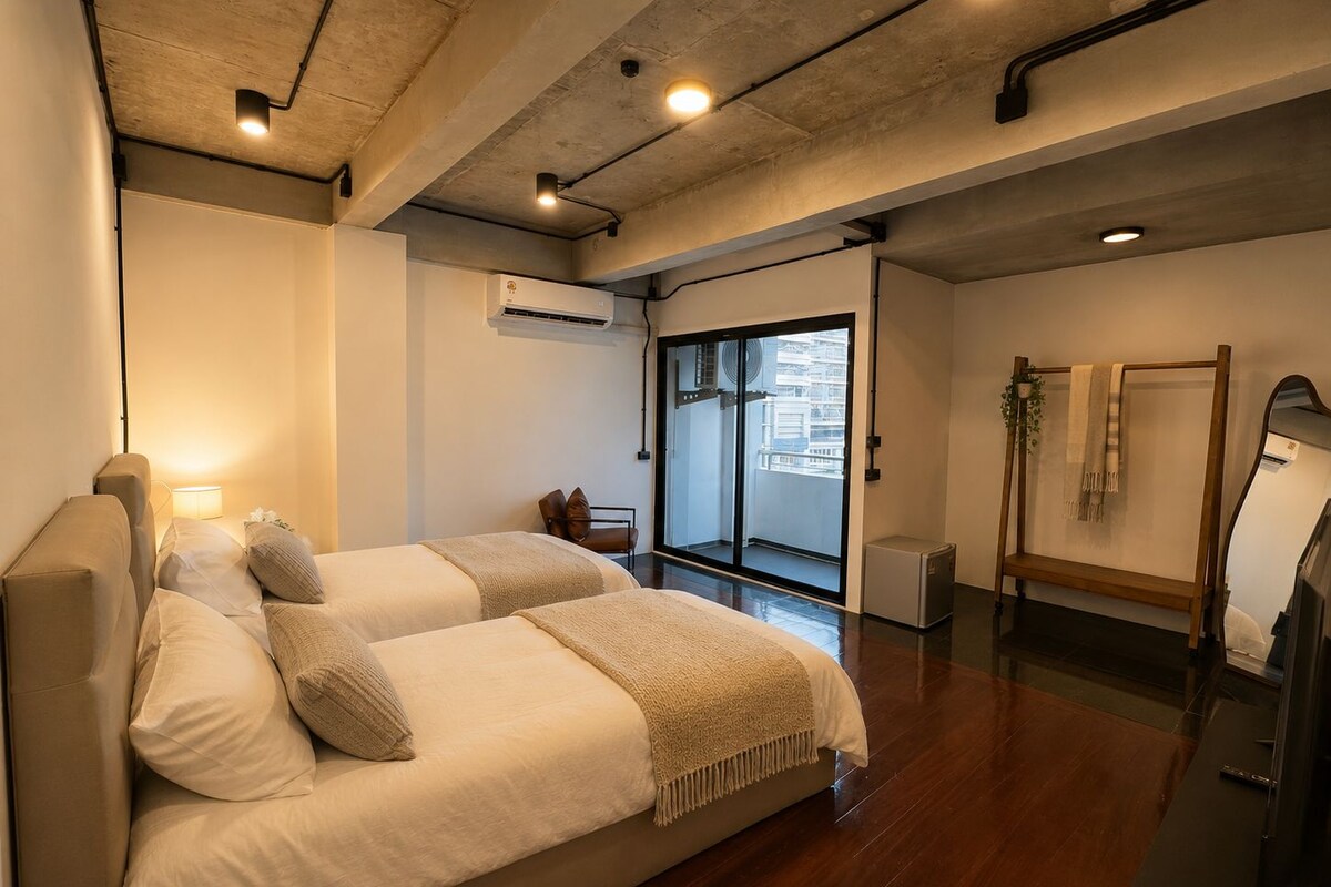 A hotel room with a bed, a small table, a mirror, and a view of the city.