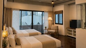 Habitación de hotel con dos camas, un televisor, una mesita con lámpara y vistas a la ciudad.
