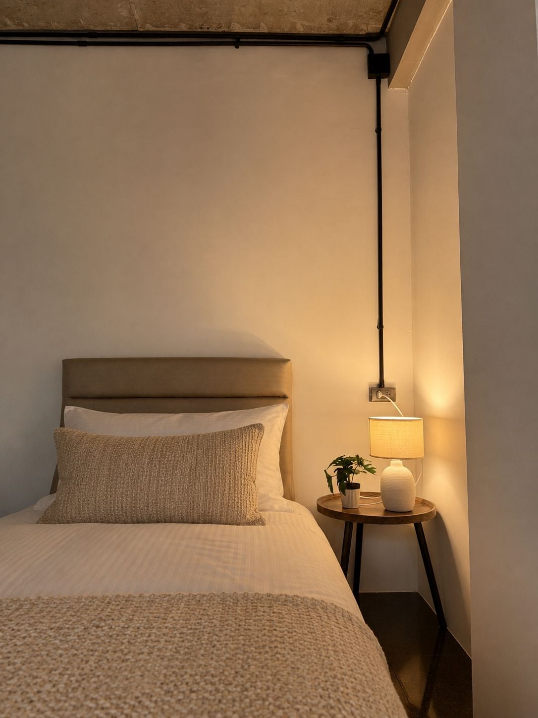 Une chambre à coucher avec un lit, des oreillers, une table de chevet avec une lampe et une prise de courant fixée au mur.