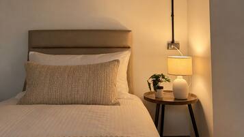 Une chambre à coucher avec un lit, des oreillers, une table de chevet avec une lampe et une prise de courant fixée au mur.