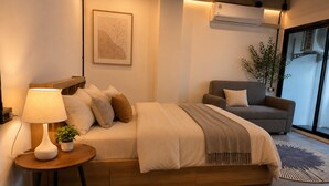 Un dormitorio moderno con cama, mesita de noche, lámpara y un sofá.