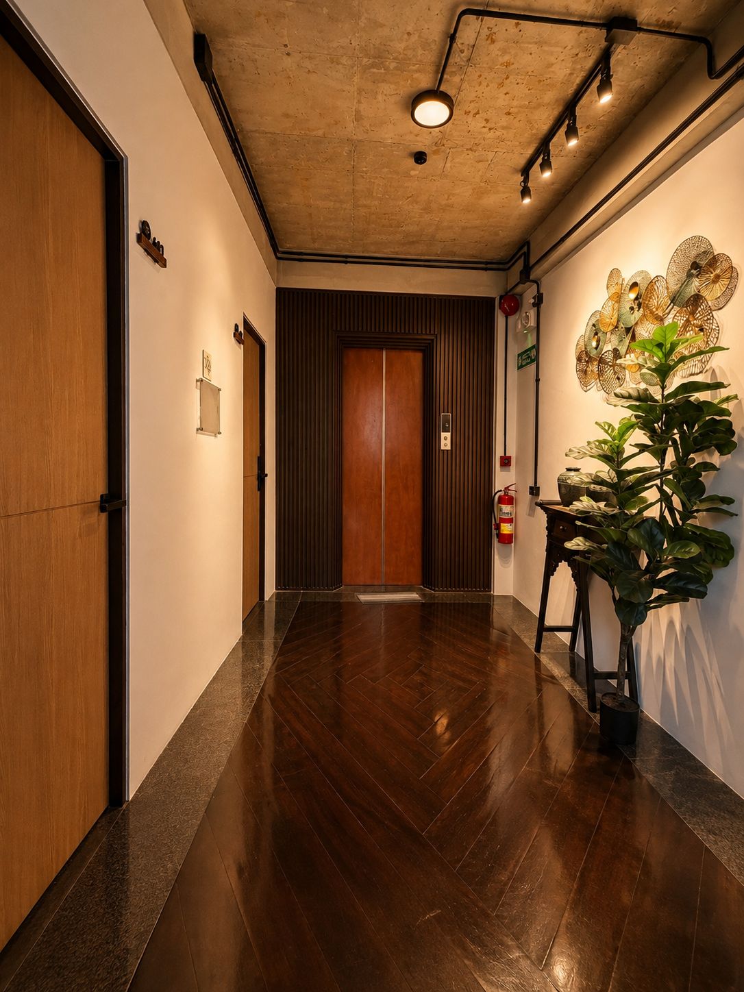 Un pasillo con una puerta de madera, una lámpara de pared y una planta en maceta.
