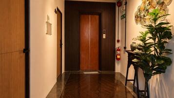 Un pasillo con una puerta de madera, una lámpara de pared y una planta en maceta.