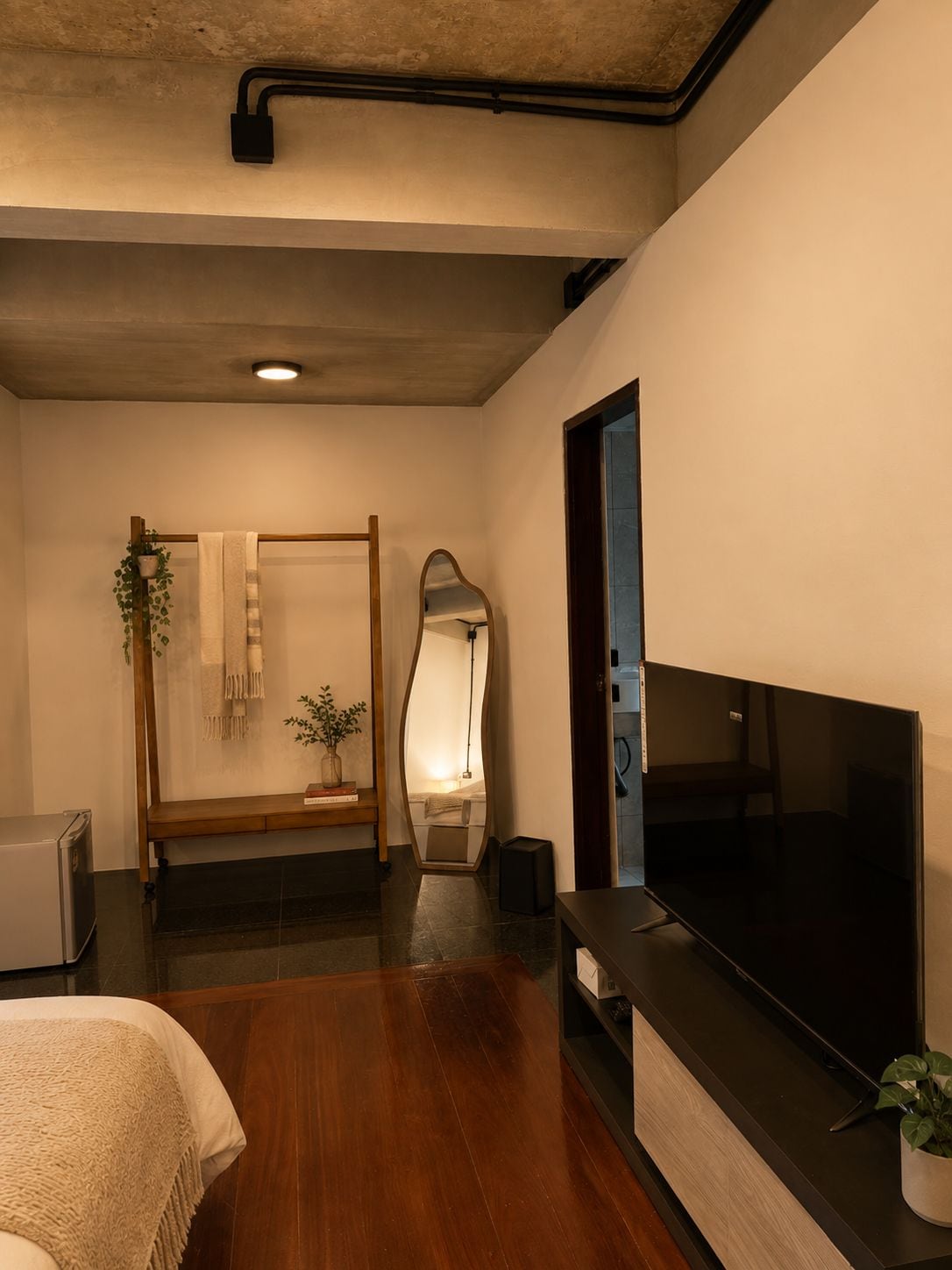 Un baño moderno con un banco de madera, un espejo, un perchero y una planta en maceta.