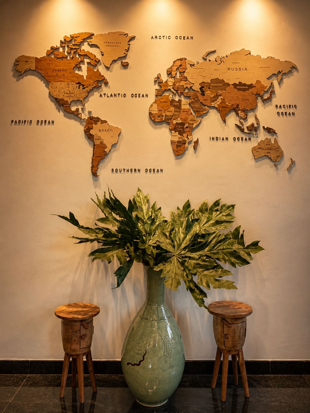 A world map on a wall with a green vase and two wooden stools in front.