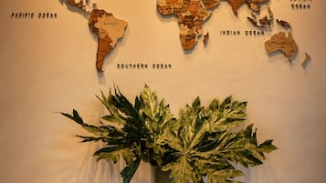 A world map on a wall with a green vase and two wooden stools in front.