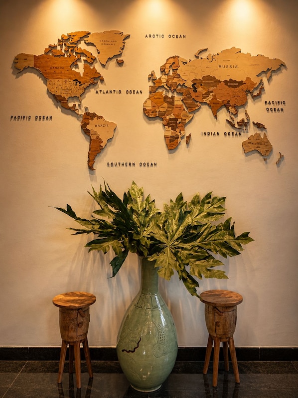 Un mapa mundial en la pared, con un jarrón verde y dos taburetes de madera al frente.
