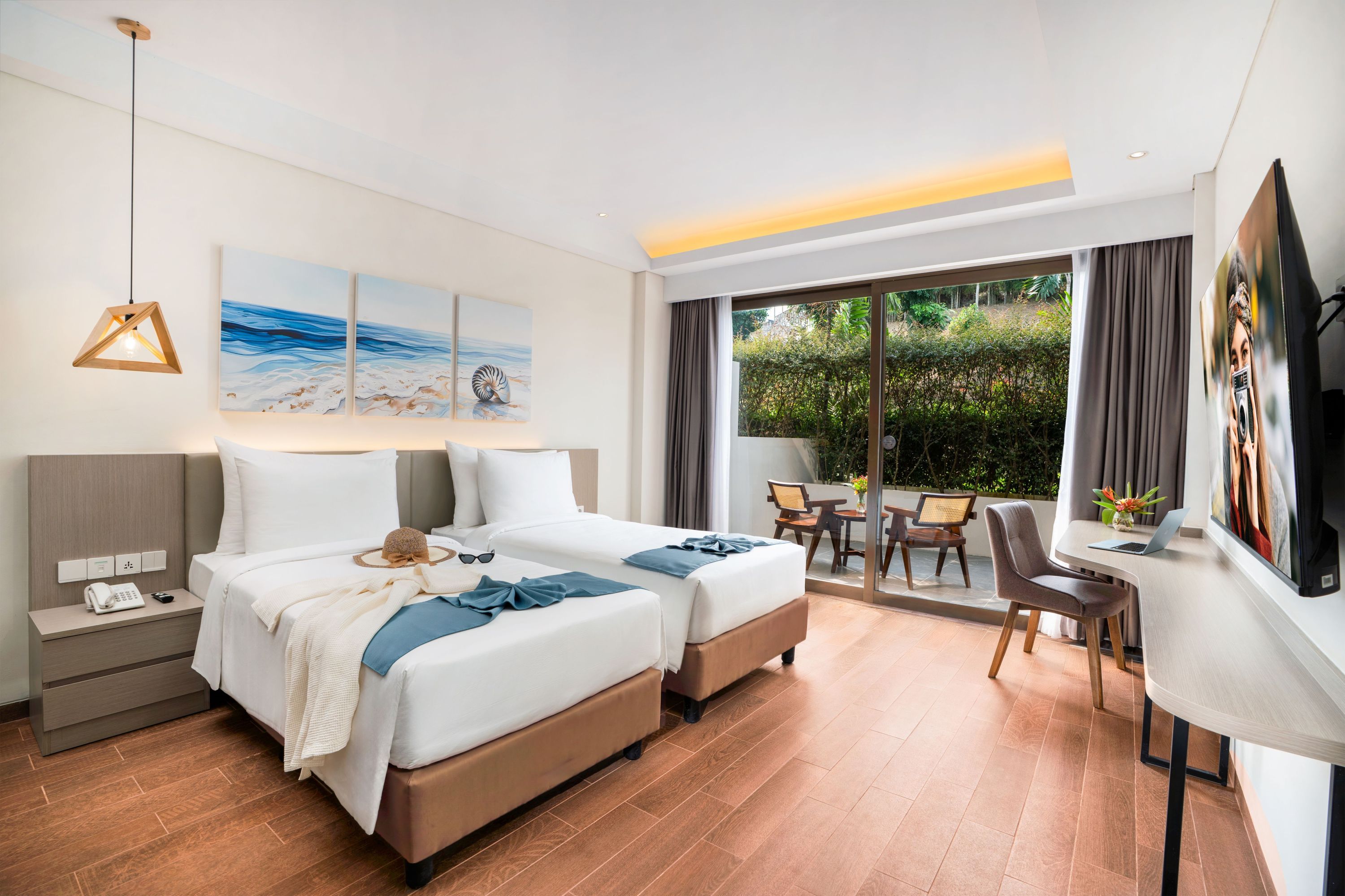 Une chambre d’hôtel avec deux lits, un bureau, une chaise, une télévision et un balcon donnant sur un espace verdoyant.