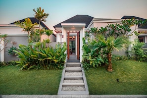A modern house with a well-maintained garden, a paved pathway leading to the entrance, and a clear sky.