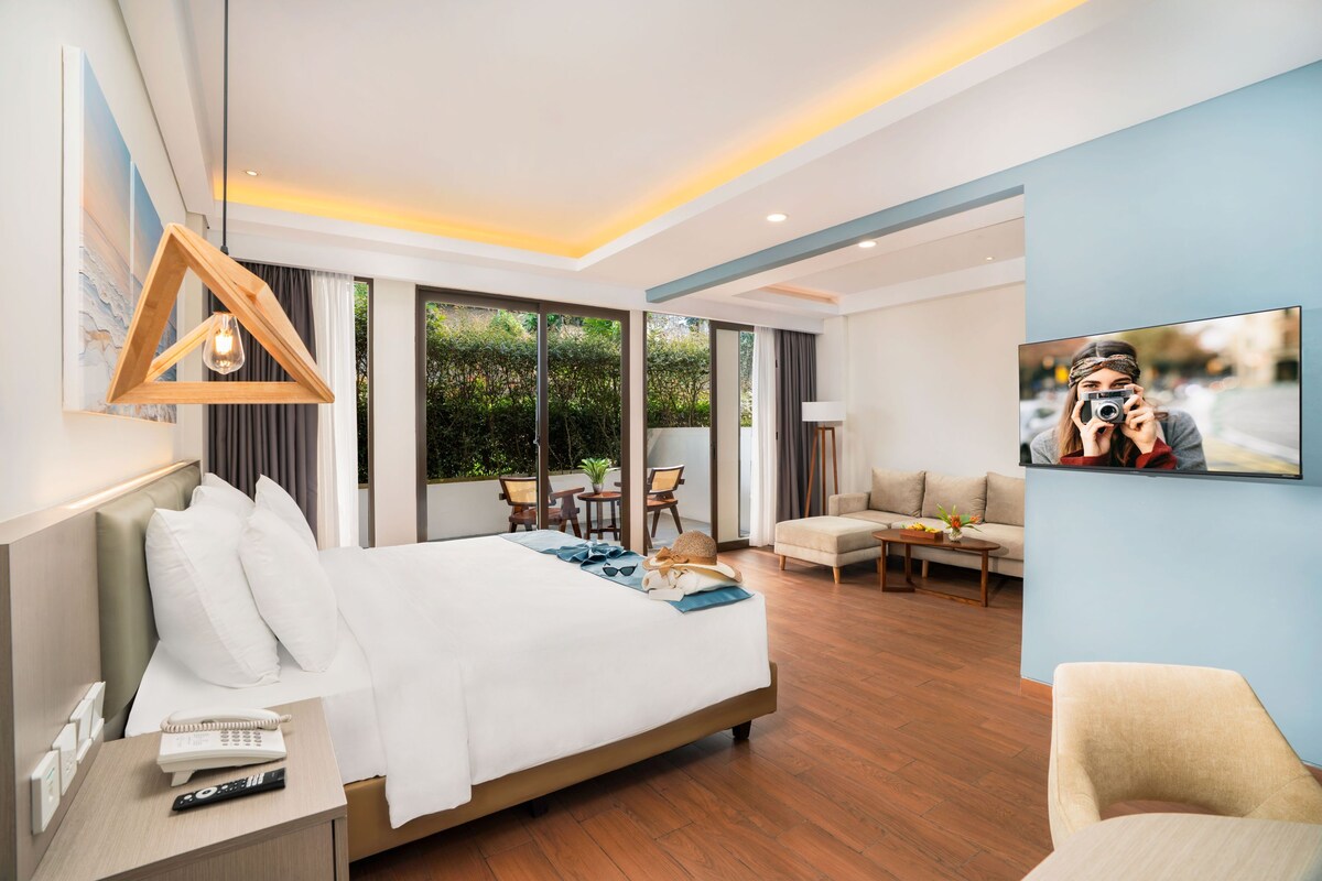 A modern hotel room with a large bed, a desk with a phone and remote, a seating area with a sofa and chairs, and a television on the wall.