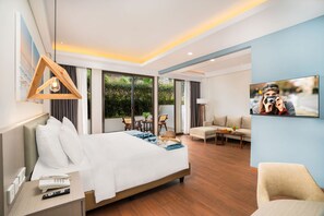 A modern hotel room with a large bed, a desk with a phone and remote, a seating area with a sofa and chairs, and a television on the wall.