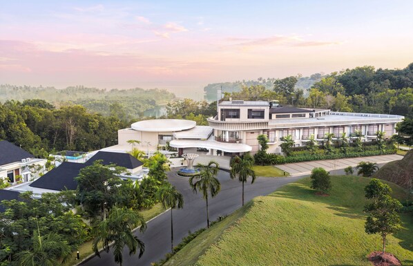 A modern hotel with a central courtyard, surrounded by lush greenery and a view of a body of water.