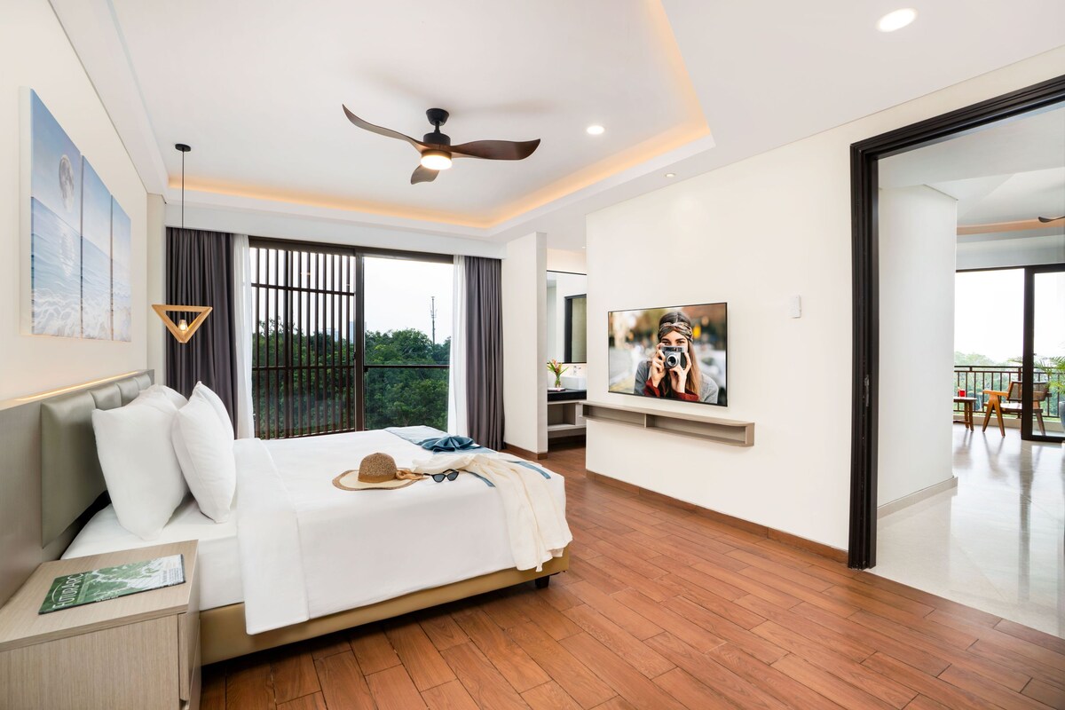 A modern hotel room with a large bed, a ceiling fan, a TV, and a balcony with outdoor furniture.
