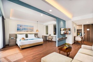 A modern hotel room with a bed, desk, TV, and seating area.