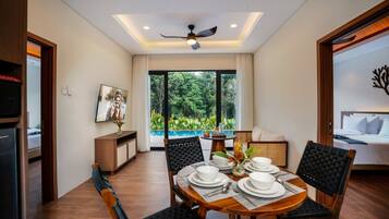 Un coin repas avec une table dressée pour quatre personnes, un ventilateur de plafond et une vue sur une piscine, visible à travers de grandes fenêtres.