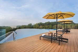 A wooden deck with a pool, lounge chairs, and umbrellas.