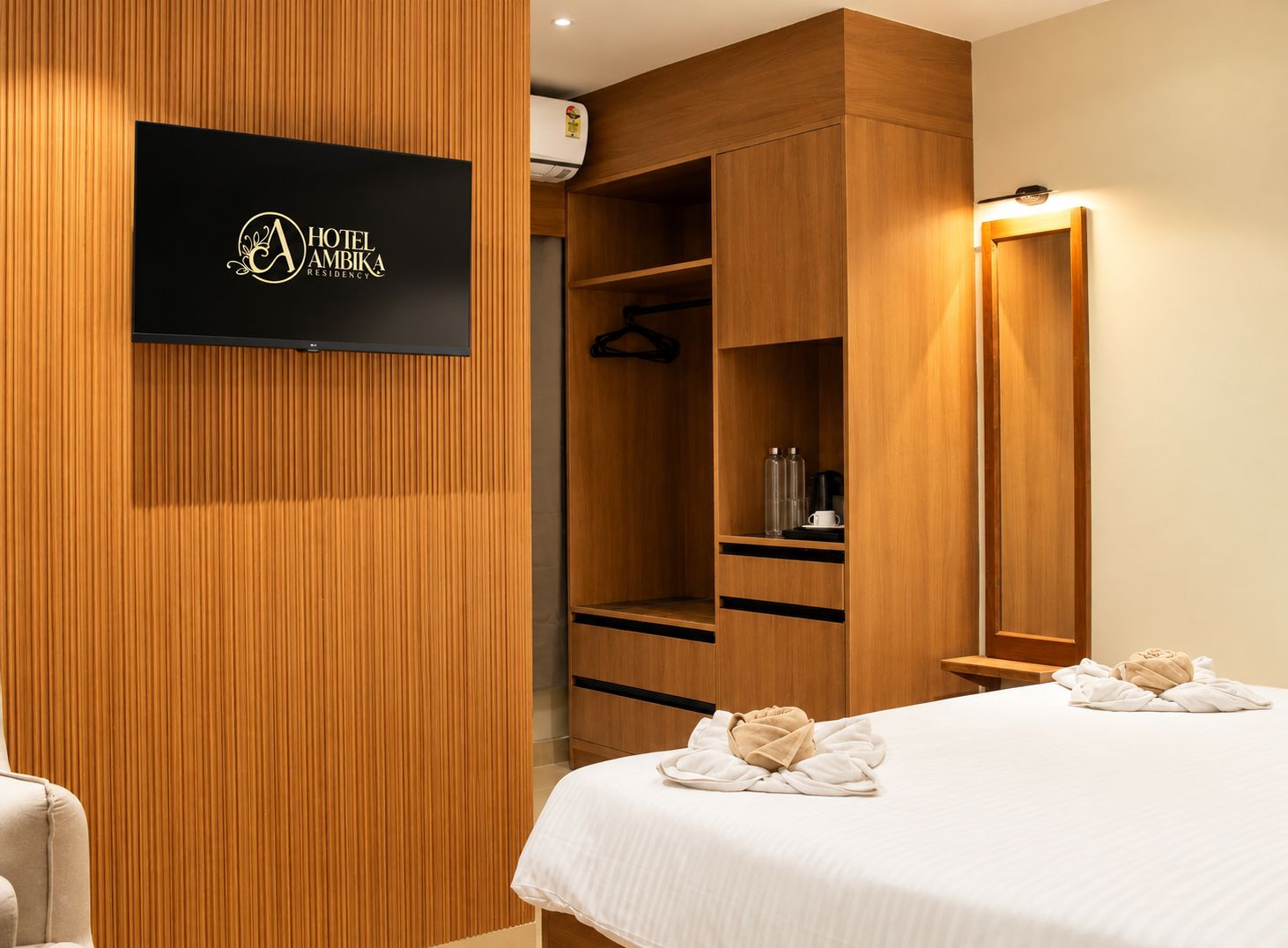 Ein Hotelzimmer mit einem Holzschrank, einem Bett mit Handtüchern und einem an der Wand befestigten Flachbildfernseher.