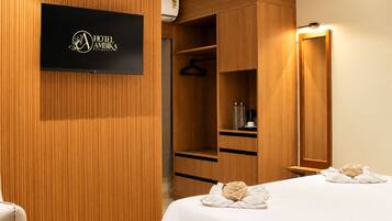 Ein Hotelzimmer mit einem Holzschrank, einem Bett mit Handtüchern und einem an der Wand befestigten Flachbildfernseher.