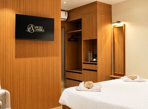 Habitación de hotel con armario de madera, cama con toallas y televisor de pantalla plana montado en la pared.