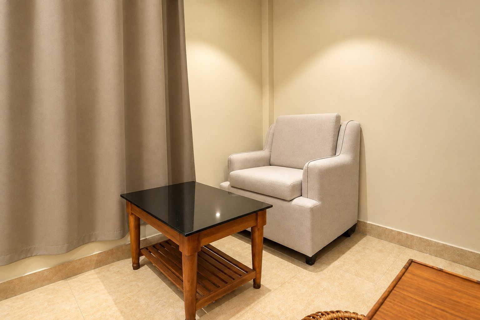 Une pièce avec une table noire, un fauteuil gris et un rideau.