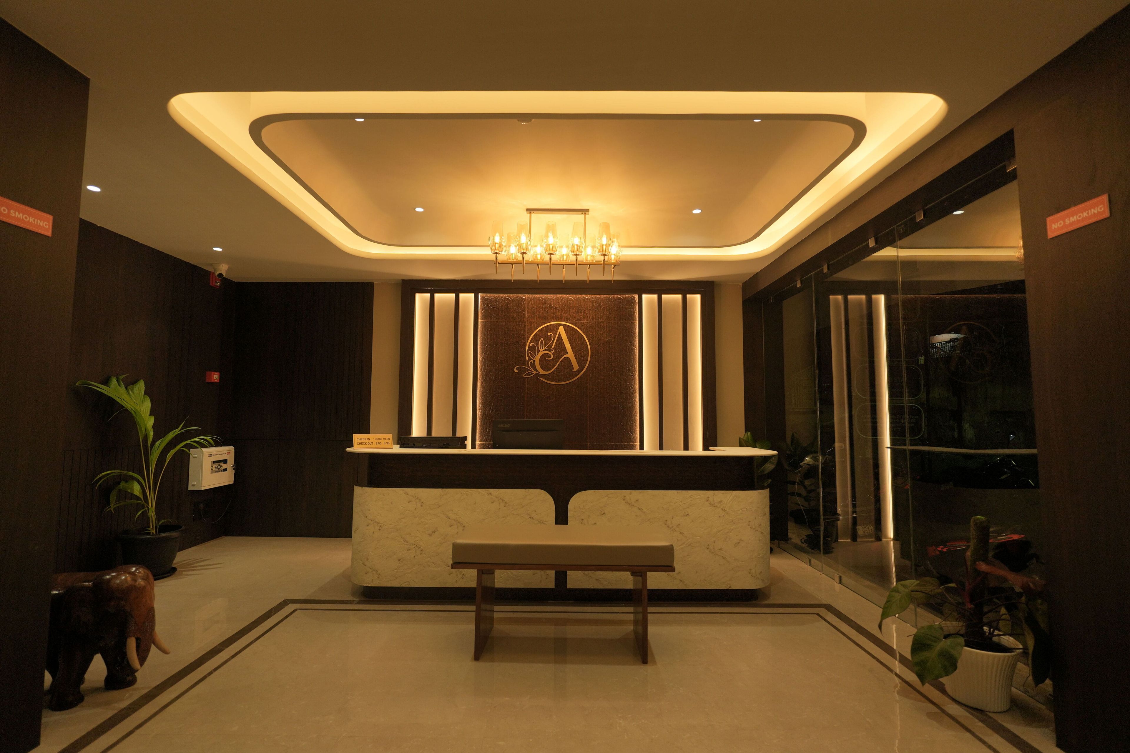 A hotel reception area with a marble counter, a chandelier, a large mirror, and a bench.