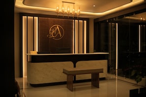 A reception desk with a marble top, a bench in front, and a wall-mounted logo.