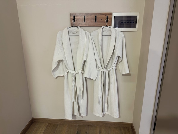 Two white bathrobes hanging on a wooden rack against a wall with a wooden floor.
