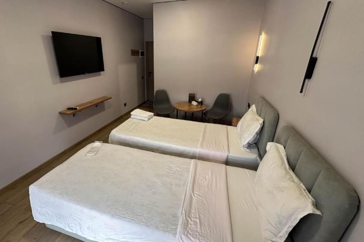A hotel room with two beds, a TV, a small table, and two chairs.