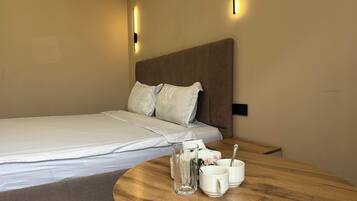A neatly made bed with pillows, a bedside table with a glass pitcher and two cups, and two wall-mounted light fixtures.