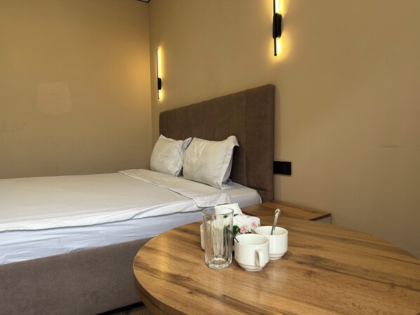 A neatly made bed with pillows, a bedside table with a glass pitcher and two cups, and two wall-mounted light fixtures.