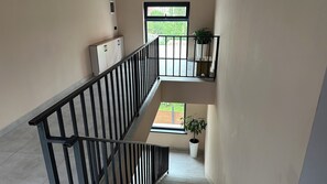 A multi-level interior with a staircase, a window with a view of greenery, and a potted plant.