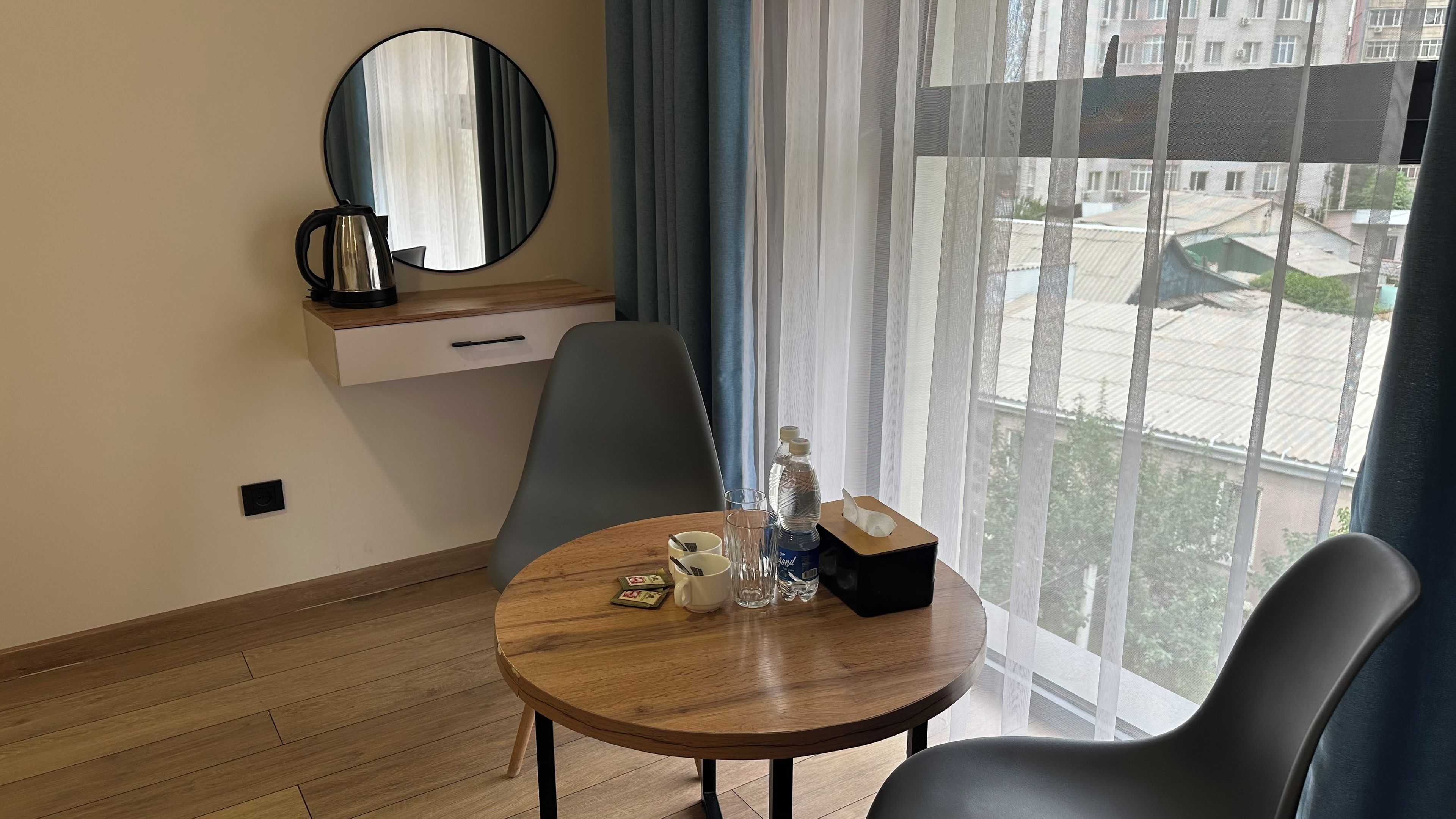 A hotel room with a round wooden table, two chairs, a coffee maker, a bottle of water, and a tissue box.