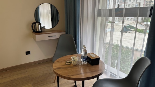 A hotel room with a round wooden table, two chairs, a coffee maker, a bottle of water, and a tissue box.