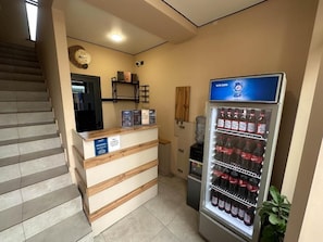 A reception area with a counter, a refrigerator stocked with beverages, and a staircase.