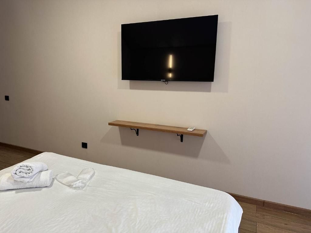 Una camera d'albergo con un letto, una televisione a schermo piatto fissata al muro e uno scaffale in legno sotto la TV.
