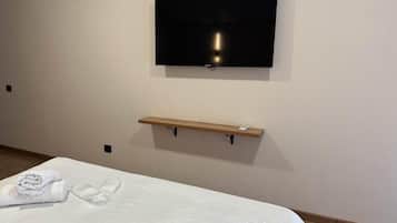 Una camera d'albergo con un letto, una televisione a schermo piatto fissata al muro e uno scaffale in legno sotto la TV.