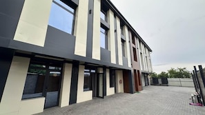 A modern building with a flat roof, large windows, and a paved entrance area.
