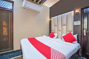 Ein Hotelzimmer mit Bett, Wandklimaanlage, Tür mit Griff und Lichtschalter an der Wand.