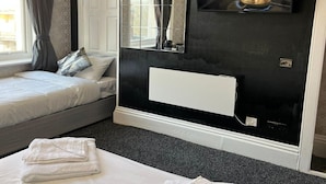 Ein Schlafzimmer mit Bett, Nachttisch, Spiegel, Fernseher und Heizkörper.
