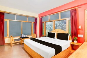 Habitación de hotel con una cama grande, un escritorio de madera, una silla y una ventana con cortinas.