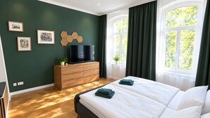 Ein Schlafzimmer mit einem großen Bett, einem Fernseher auf einer Holzkommode und einem Fenster mit Vorhängen.